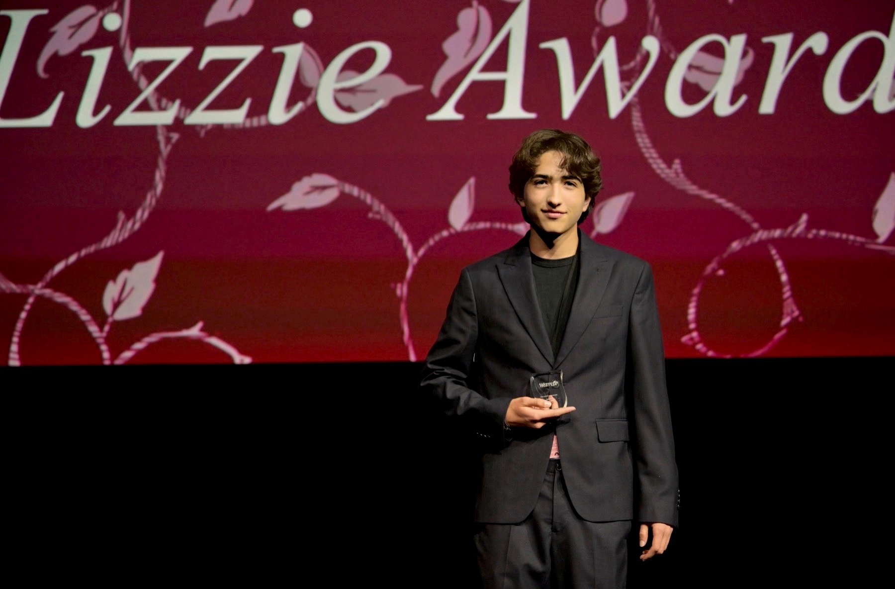 Hudson Hillin on stage holding an award at the Westflix Lizzie Awards